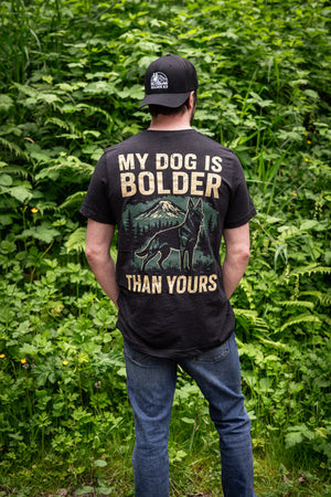 Person wearing 'My Dog Is Bolder Than Yours' t-shirt in a natural outdoor setting, showcasing the bold design.