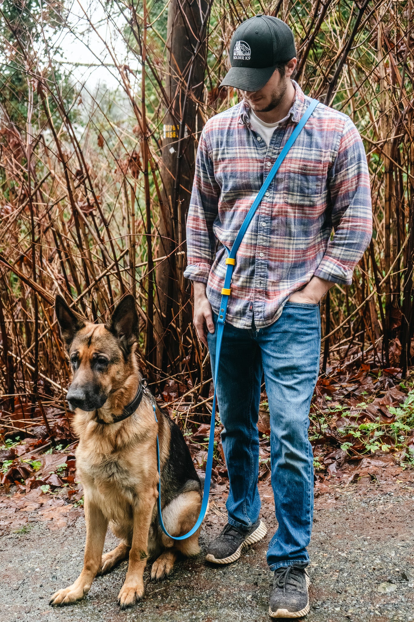 Person walking a German Shepherd dog with an adjustable length hands-free BioThane leash in a natural setting.