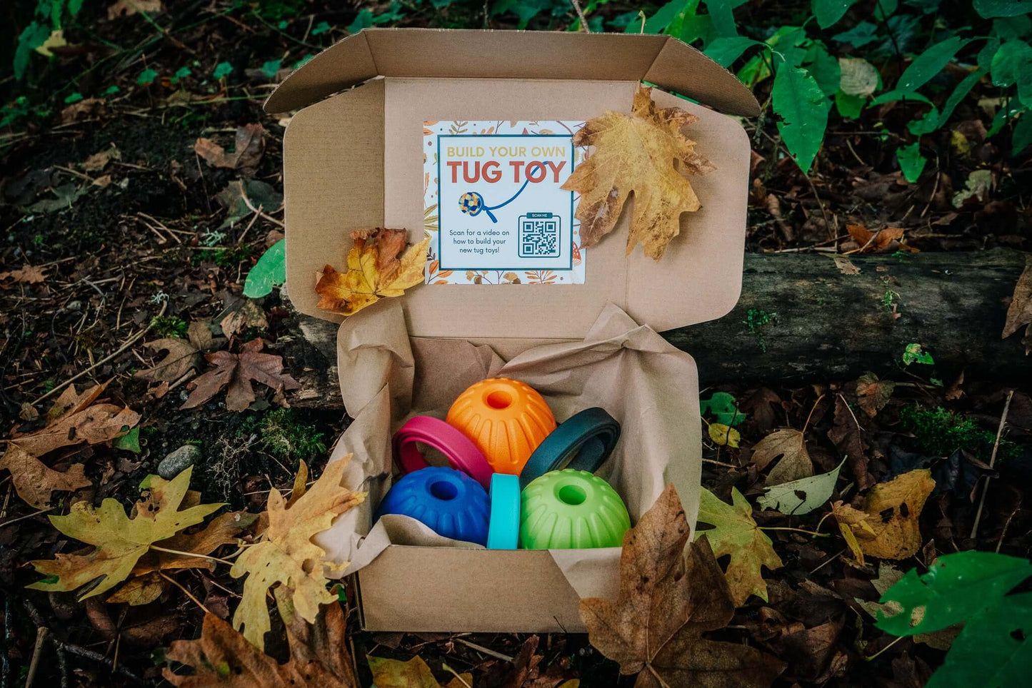 build your own tug kit cardboard box with three custom foam ball options and three custom biothane handle options sitting on a pile of leaves