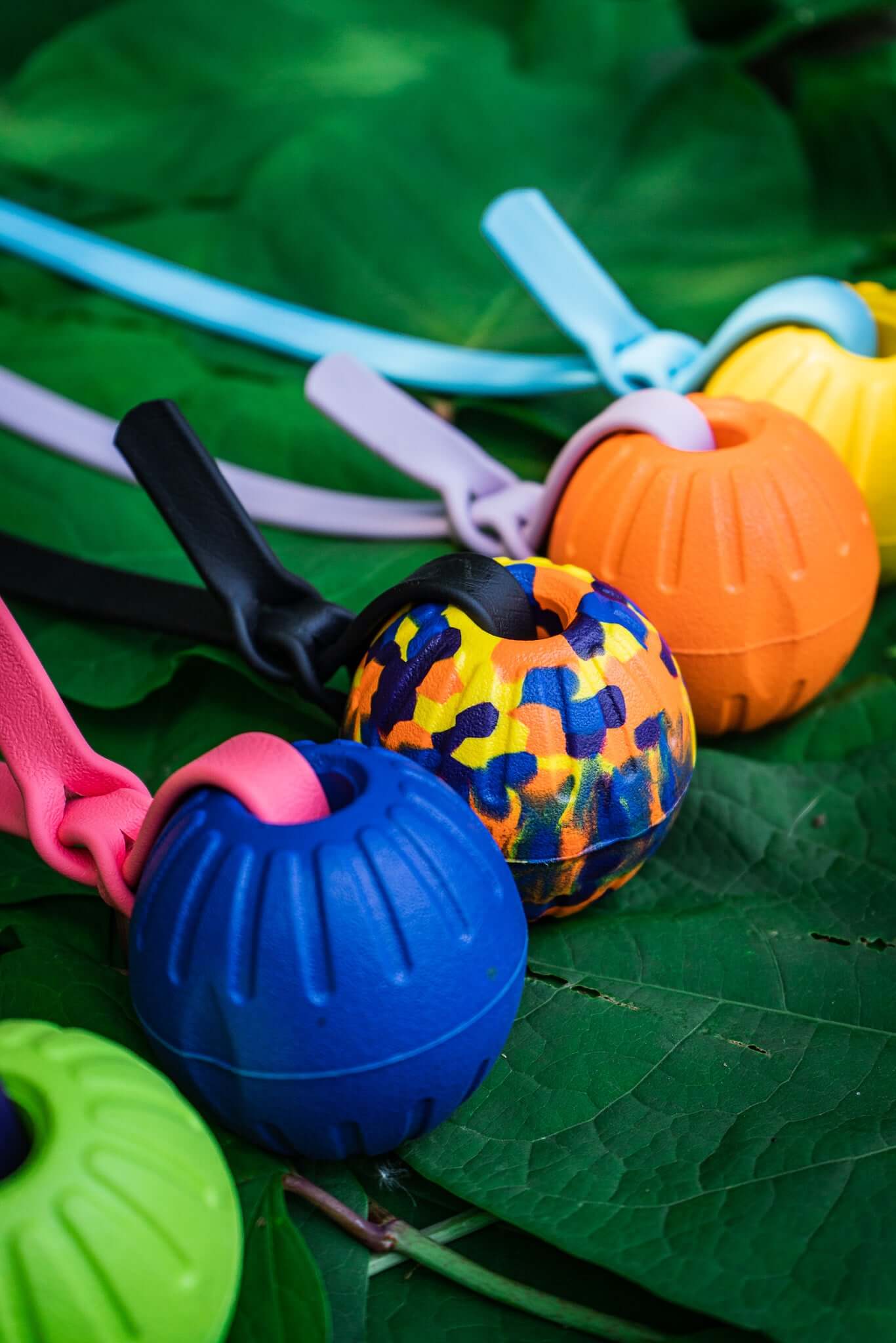 four tugs with different custom foam balls each with a different custom biothane strap of various colors on a background of leaves