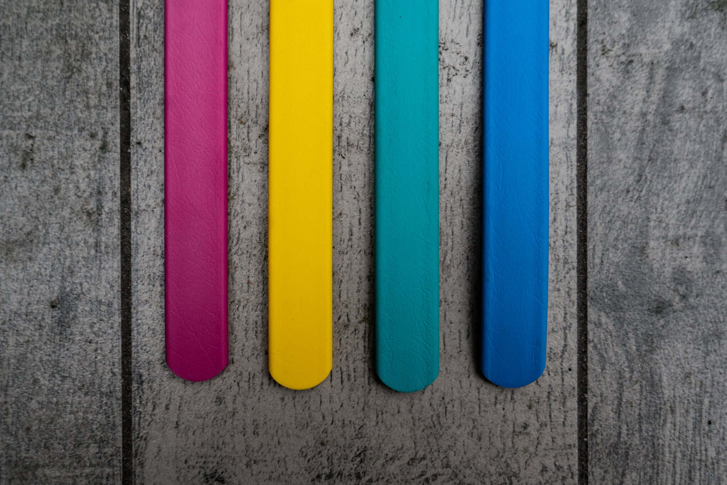 four colors of biothane tug toy straps on a wood background