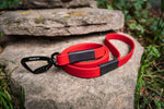 bright red biothane dog leash sewn with black carabiner on a stone background