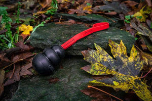 dog tug toy with a black kong toy on a bright red biothane rope on a background of leaves