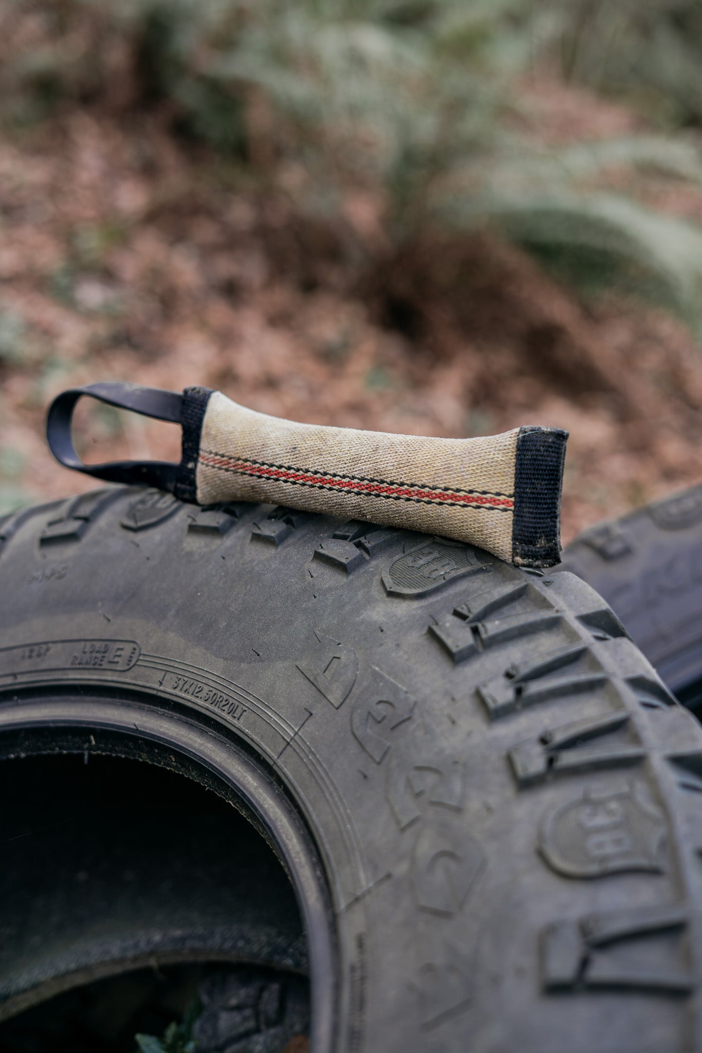 Upcycled fire hose tug toy with BioThane handle, resting on a tire, showcasing durability and eco-friendliness.