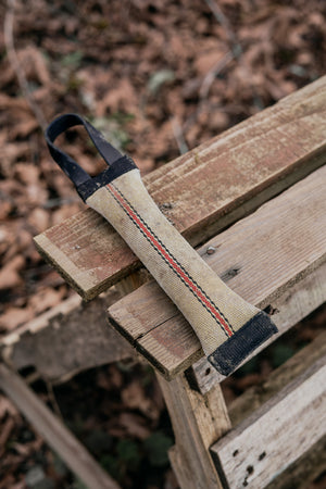 Upcycled fire hose tug for dogs resting on wooden surface, featuring a BioThane® handle and durable design.