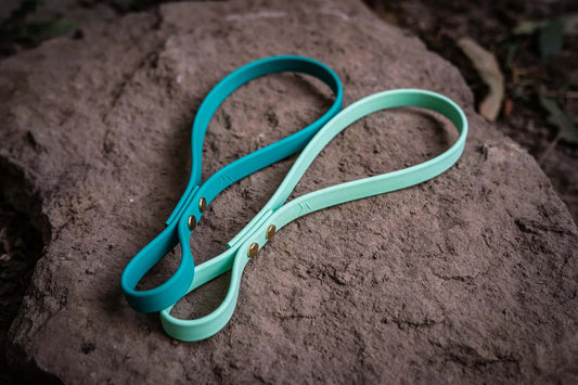 two colors of biothane tug toy replacement straps on a stone background