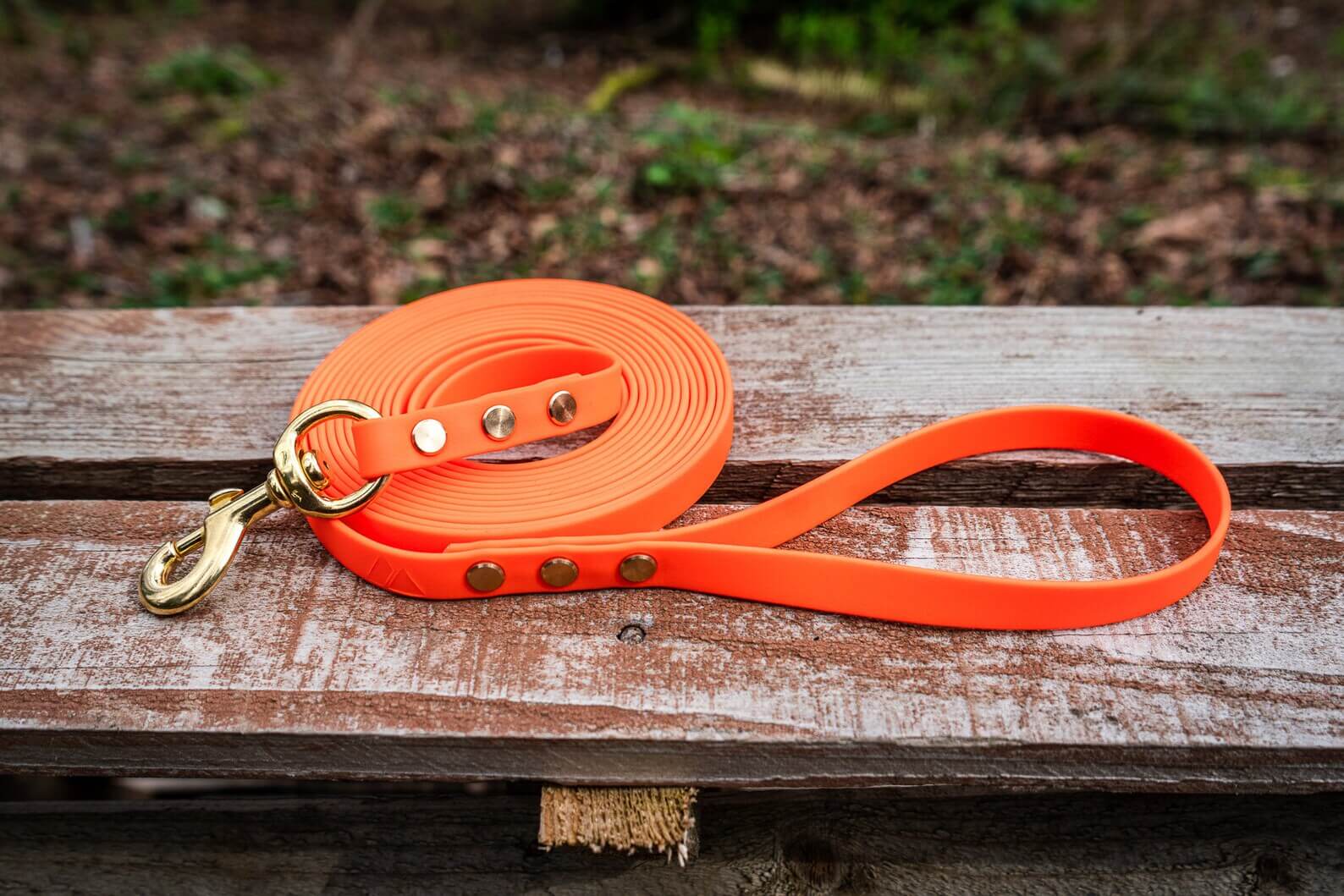 biothane long line dog leash in orange with gold hardware on a wood background