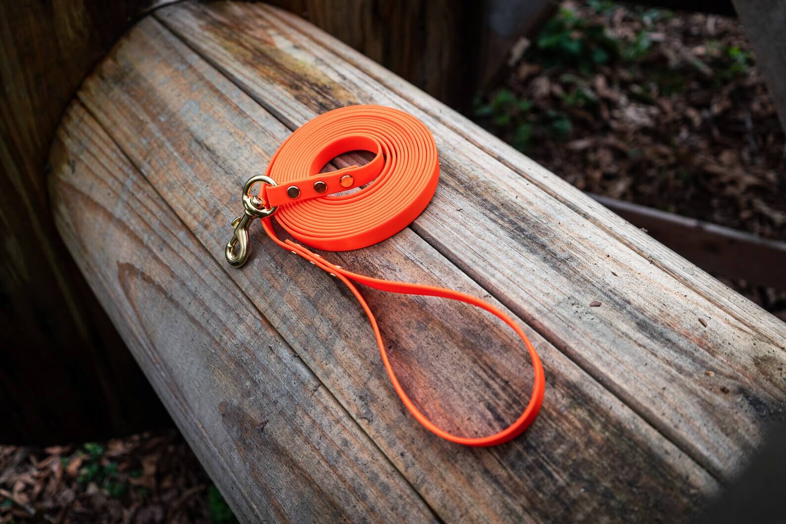 biothane long line dog leash in orange with gold hardware on a wood background
