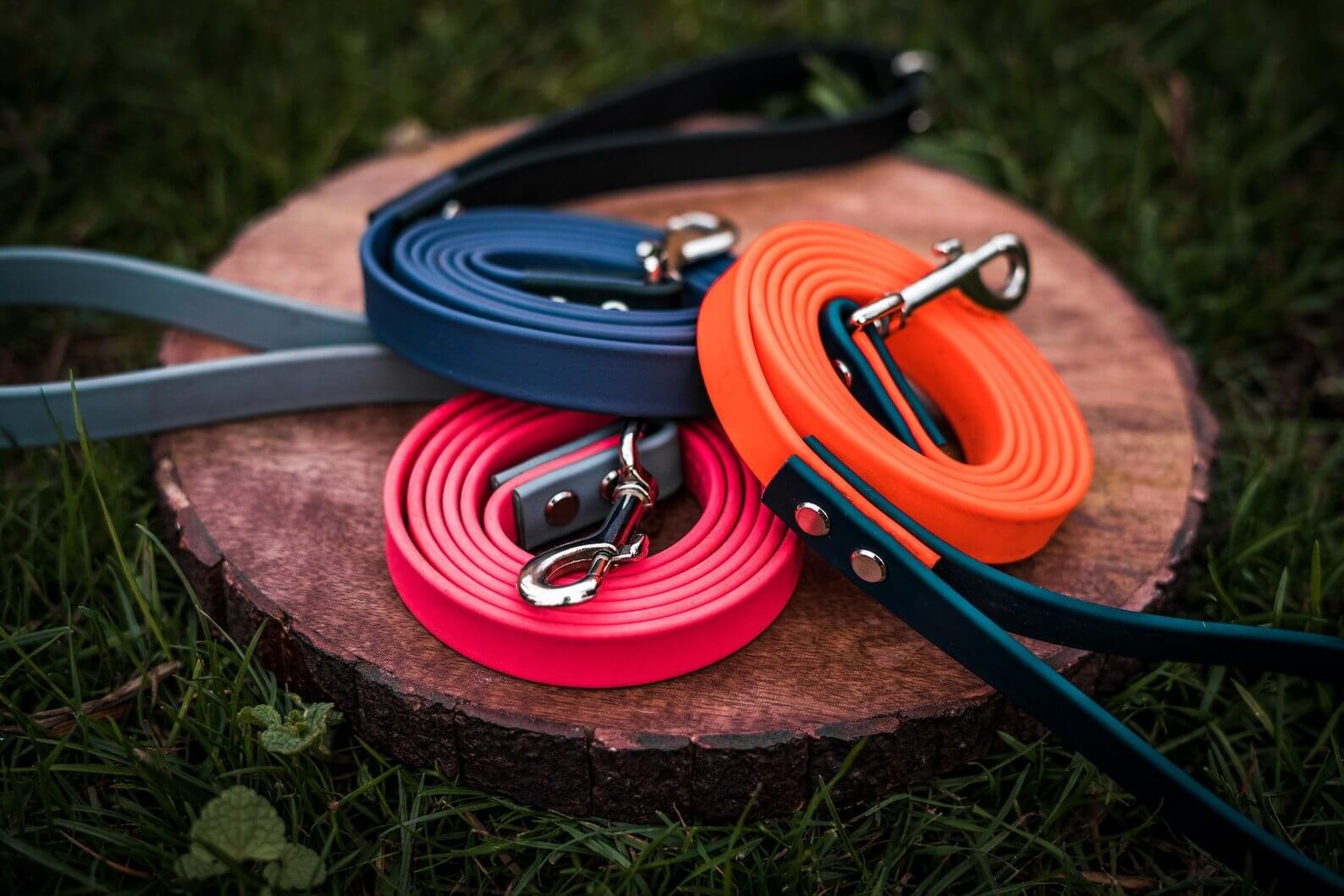 three two-tone biothane dog leashes with deep sea blue, orange, and hot pink biothane on a wooden background
