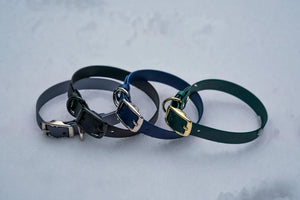 Three Voyager BioThane adjustable dog collars in black, blue, and green with heavy-duty buckles displayed on a snowy background.